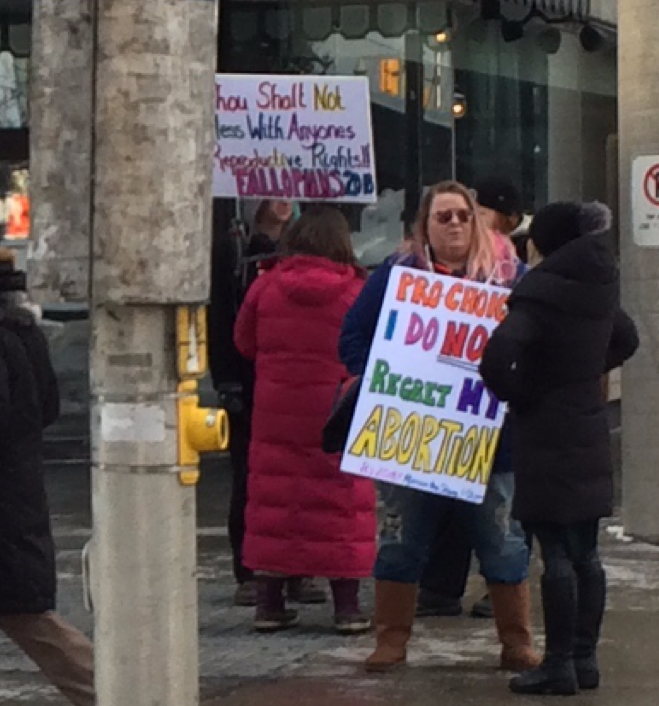 A woman in Ottawa holds a sign within an "access zone". Remove the word "NOT" and she would be arrested.